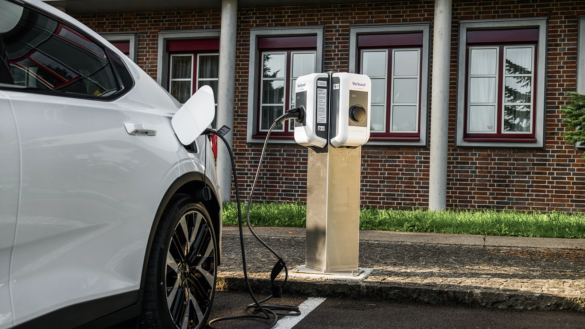 The image shows a charging station from the eCharge4Drivers project with a white electric vehicle being charged. The charging station is set against a brick wall background, and a charging cable is connected to the vehicle.